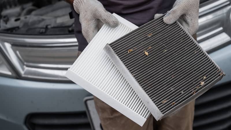 Technician holding a new and a dirty cabin air filter during a replacement service.