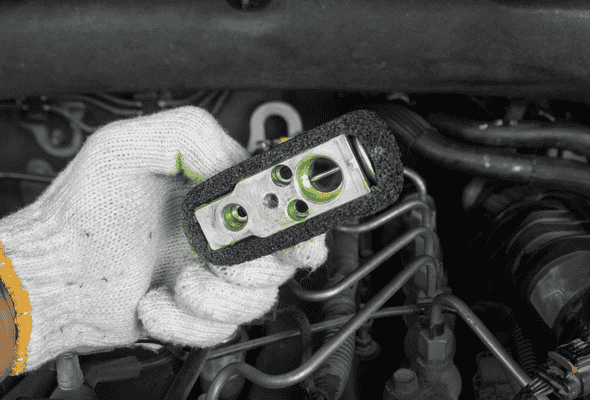 Technician inspecting a car aircon expansion valve for potential repairs. Title: Car Aircon Expansion Valve Inspection During Repair