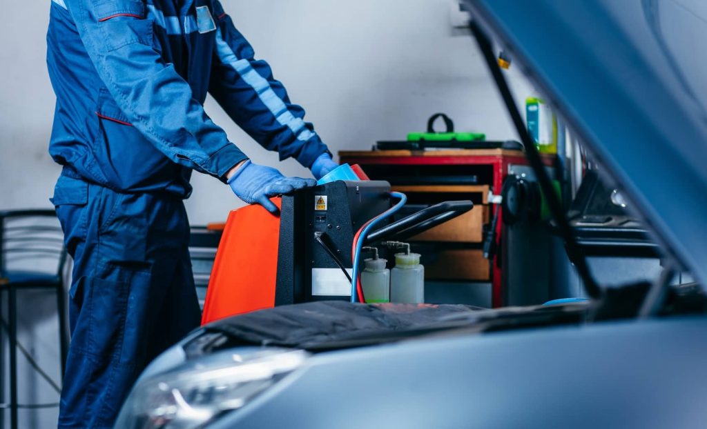 Technician performing a car air conditioning installation using specialised equipment.