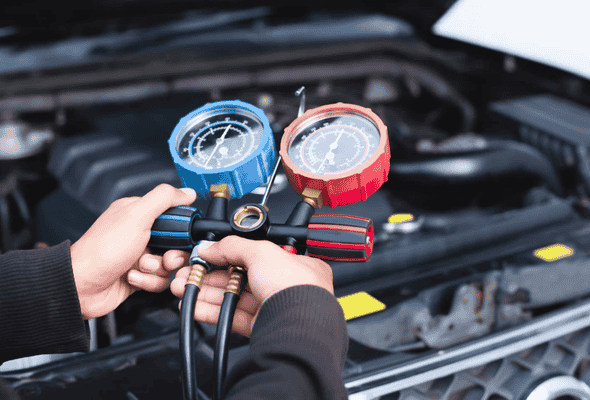 Technician using aircon pressure gauges to check car air conditioning system.