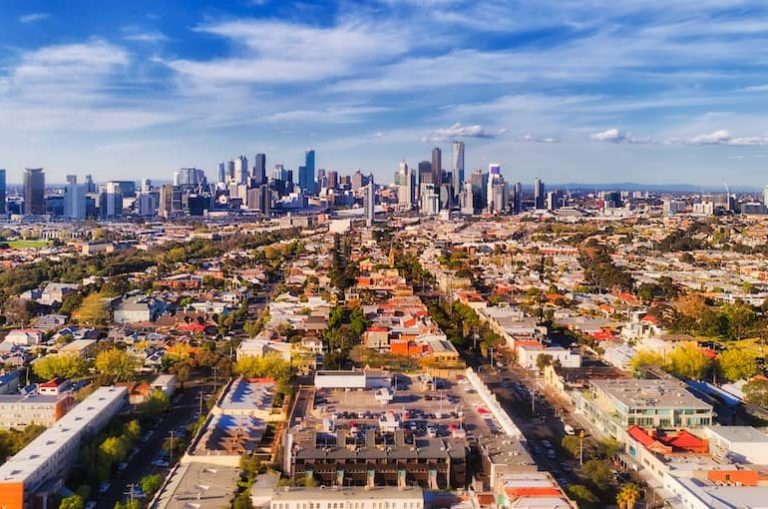 Aerial view of Melbourne city skyline with surrounding suburbs on a sunny day.