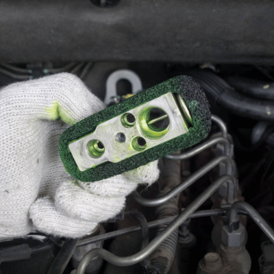 Technician inspecting a car aircon expansion valve for potential repairs. Title: Car Aircon Expansion Valve Inspection During Repair