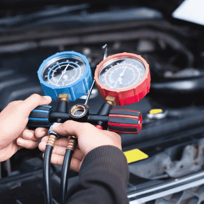 Technician using aircon pressure gauges to check car air conditioning system.