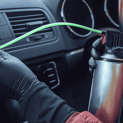 Technician using a cleaning solution to sanitise car air conditioning vents during an aircon cleaning service.